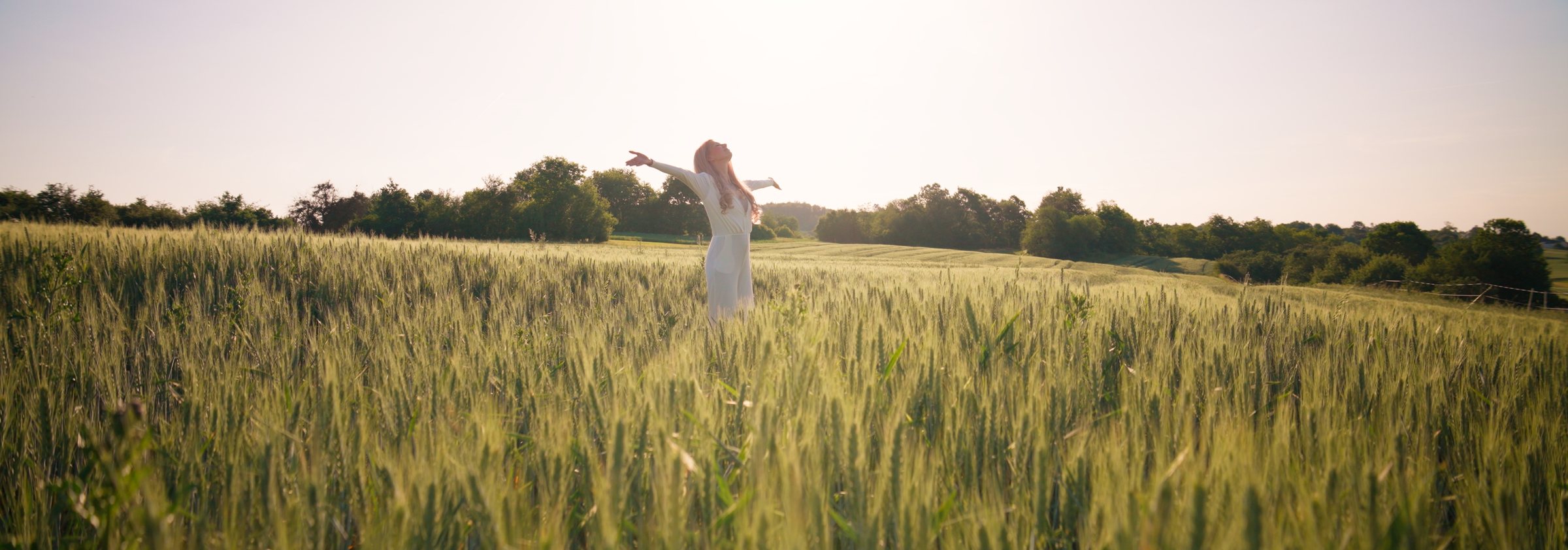 Anny mit ausgebreiteten Armen im Feld, im Gegenlicht der Abendsonne